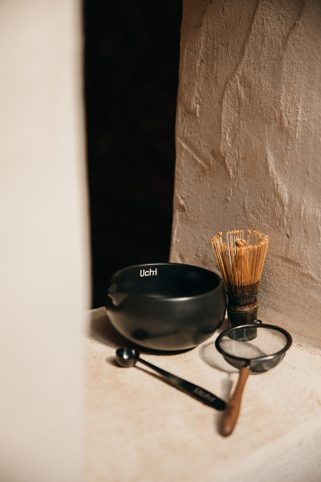 Tea and matcha making tools including a black bowl, whisk, and spoon. Uchi black, wood, ceramic essentials for matcha