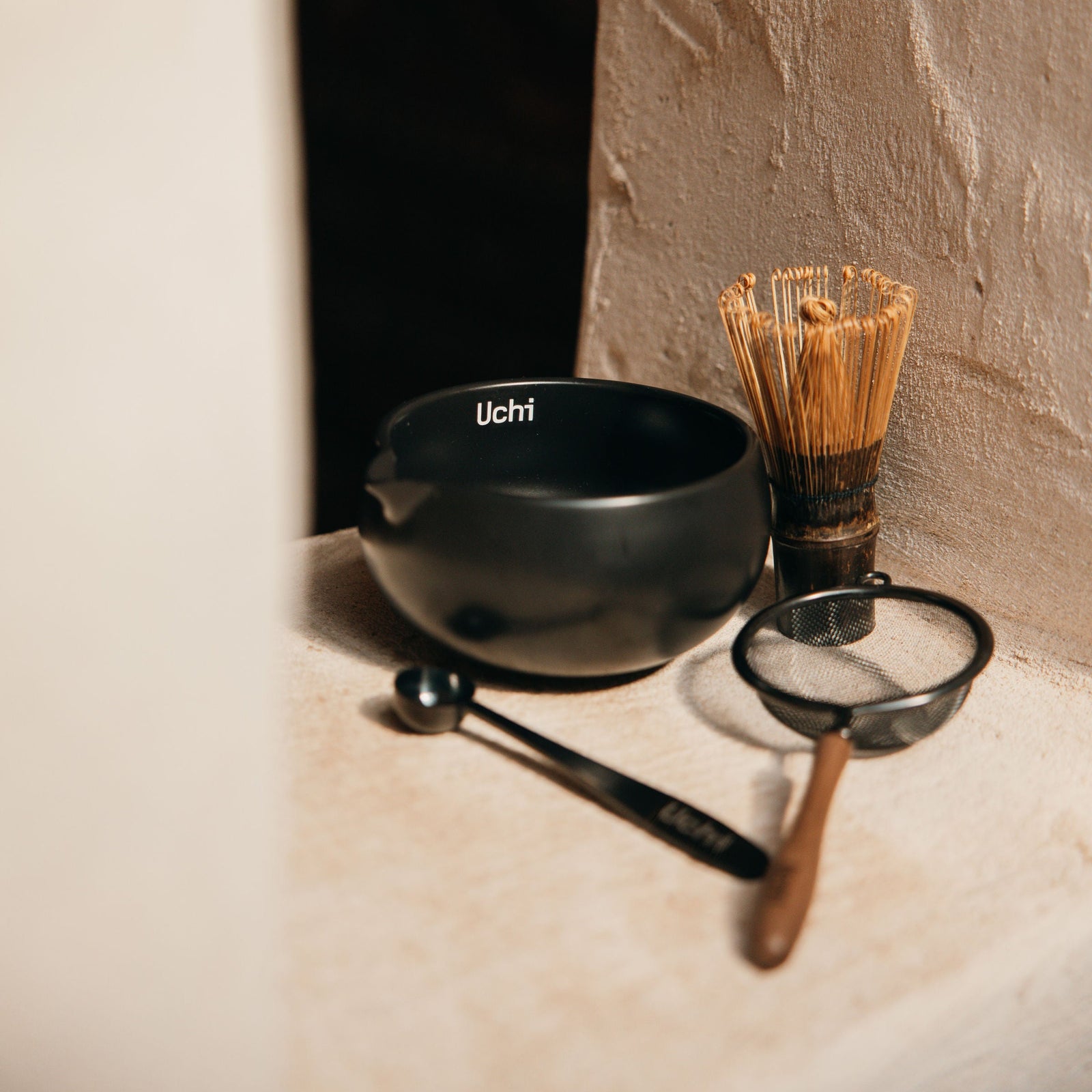 Tea and matcha making tools including a black bowl, whisk, and spoon. Uchi black, wood, ceramic essentials for matcha