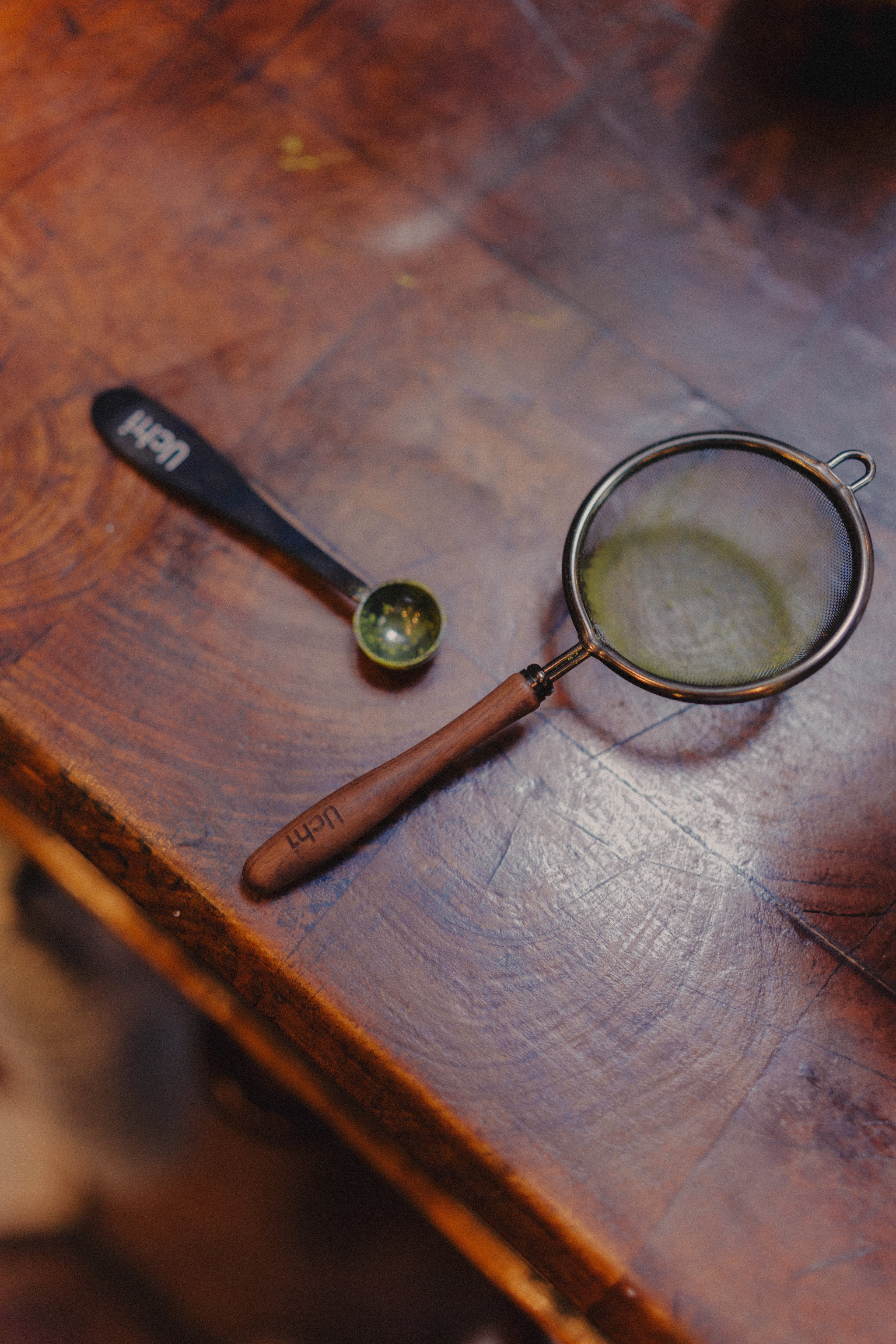 Uchi matchas Sieve close-up, fine steel mesh with wooden handle, and uchi matcha spoon on wooden background